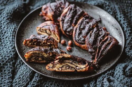 Chocolate babka slices on a black plate and a textured steel grey blanket. Tranches de babka au chocolat sur une assiette noire et une couverture gris acier texturé